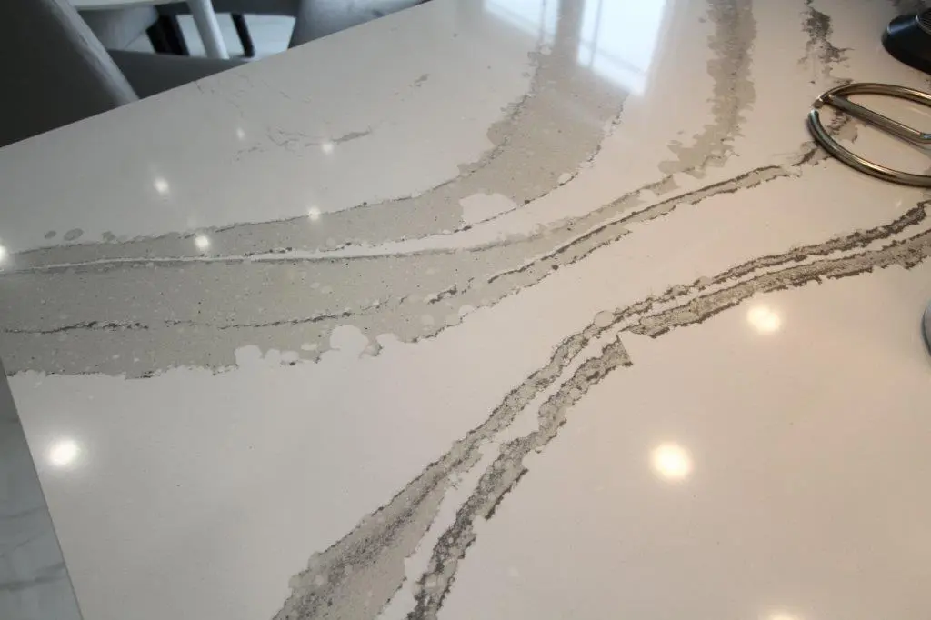 Close-up of a white quartz countertop with gray veining and subtle reflections from overhead lighting.