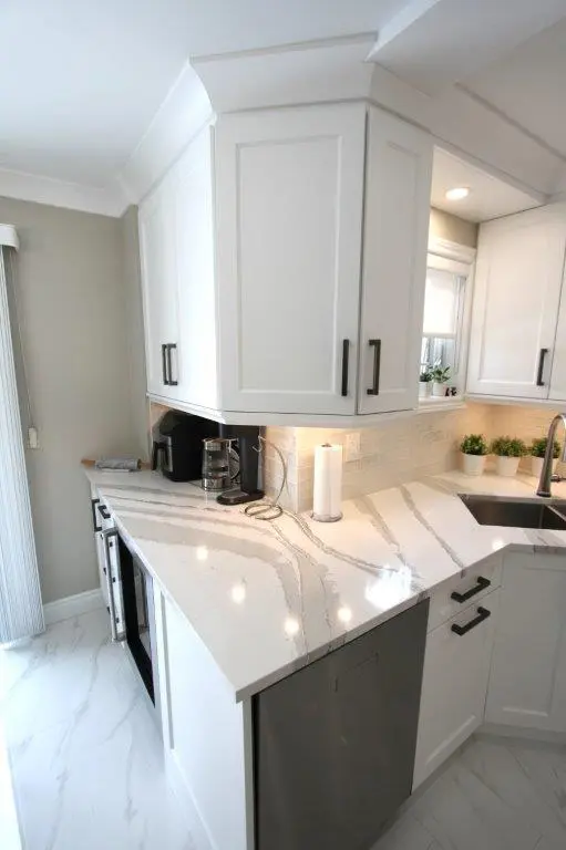 Modern kitchen corner with white cabinets, a marble-patterned countertop, stainless steel sink, and a coffee maker next to a paper towel holder.