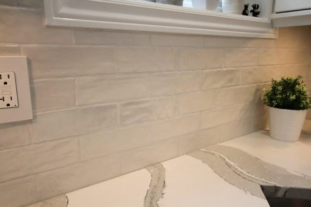 A kitchen countertop with beige subway tile backsplash, a white electrical outlet, and a small potted plant.