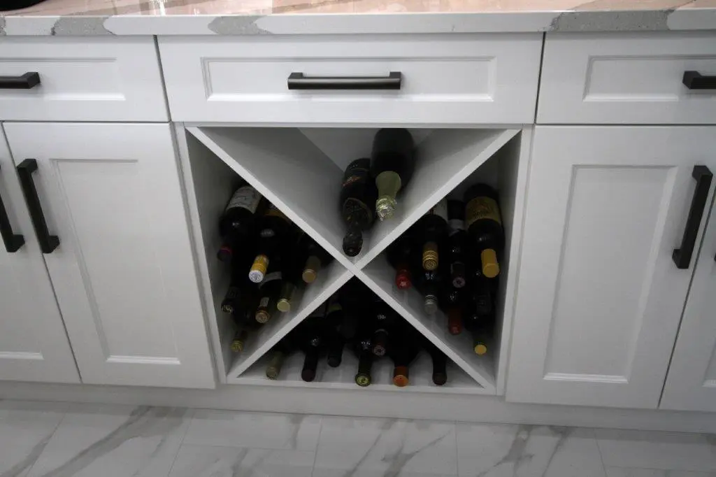 A kitchen with white cabinetry featuring a built-in diagonal wine rack filled with various wine bottles.