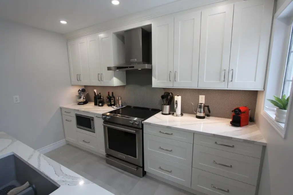 Modern kitchen with white cabinets, stainless steel appliances, and a quartz countertop, featuring a stove, microwave, and a red coffee machine.