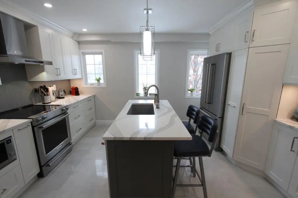 Modern kitchen with white cabinets, a central island with a quartz countertop, two black bar stools, stainless steel appliances, and a bright, airy ambiance from two large windows.