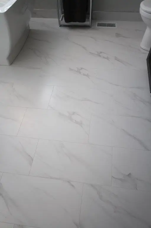 A bathroom floor with white marble-effect tiles featuring subtle gray veining.