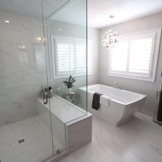 Modern bathroom featuring a glass-enclosed shower with marble-like walls, a freestanding bathtub next to a window with white shutters, a decorative pendant light, and a painting on the wall.