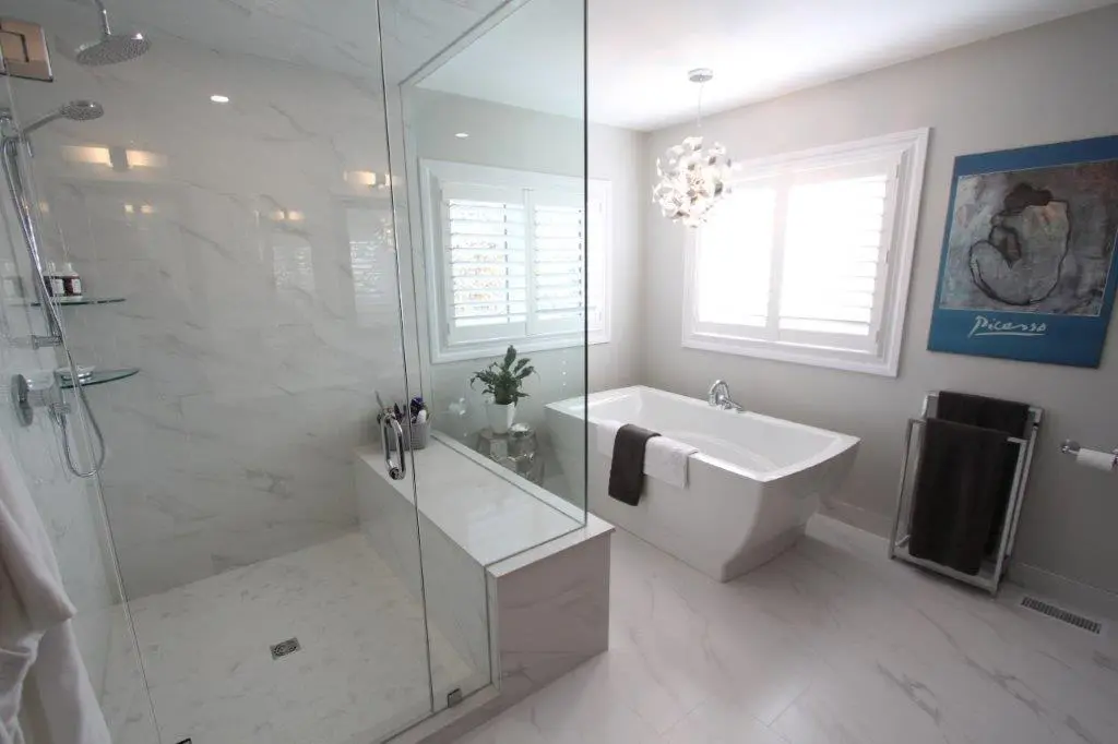 Modern bathroom featuring a glass-enclosed shower with marble-like walls, a freestanding bathtub next to a window with white shutters, a decorative pendant light, and a painting on the wall.