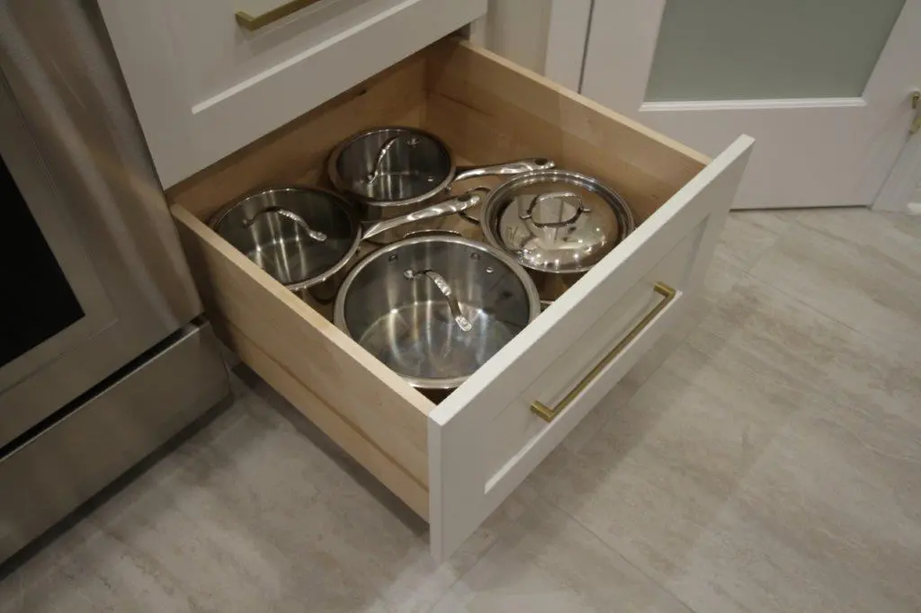 A kitchen drawer partially open, containing several stainless steel pots and pan lids neatly organized inside.