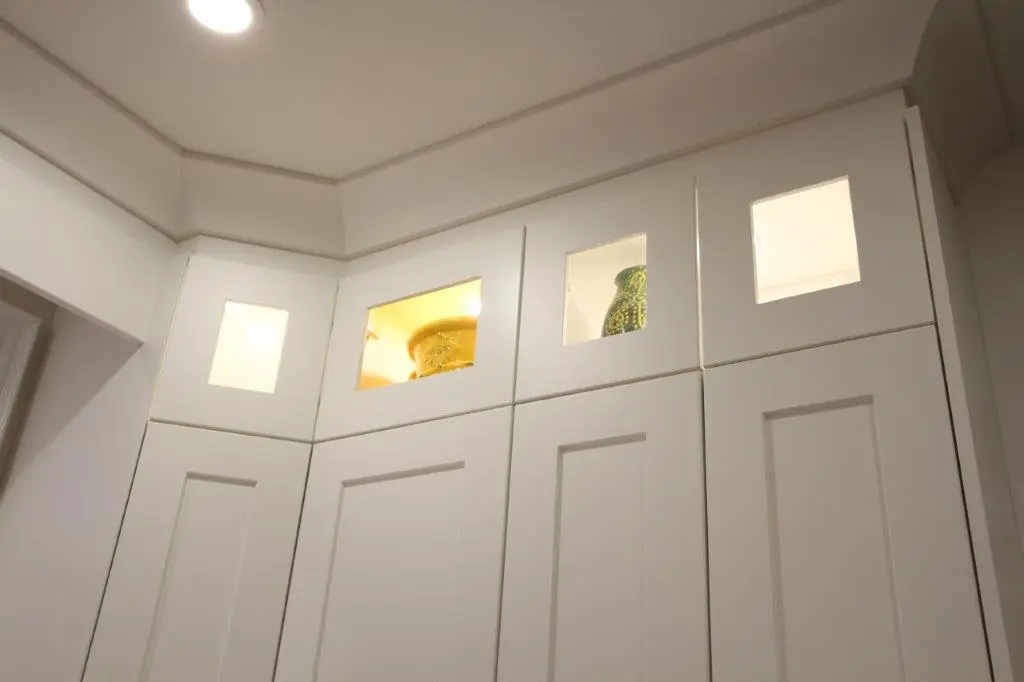 White kitchen cabinets with upper display sections featuring square windows, showcasing decorative items inside.