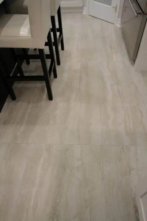 A kitchen floor with beige and light gray tiles, featuring high chairs with cream-colored seats and dark wooden legs.