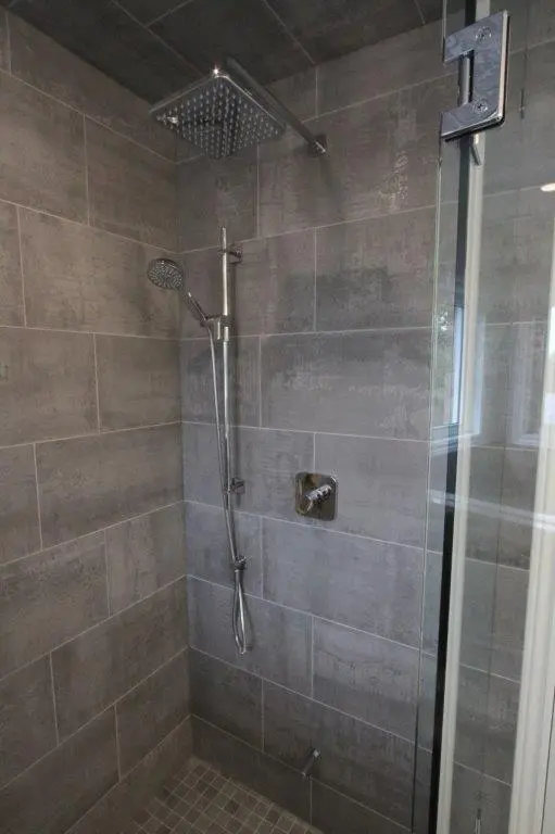 A modern shower enclosure with gray tile walls, featuring a square rainfall showerhead and a detachable handheld showerhead.