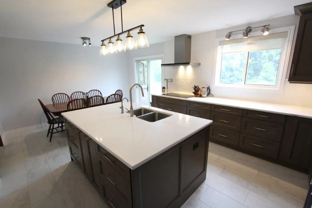Modern kitchen with a large island featuring a sink, brown cabinetry, white quartz countertops, and a dining table set in the background.
