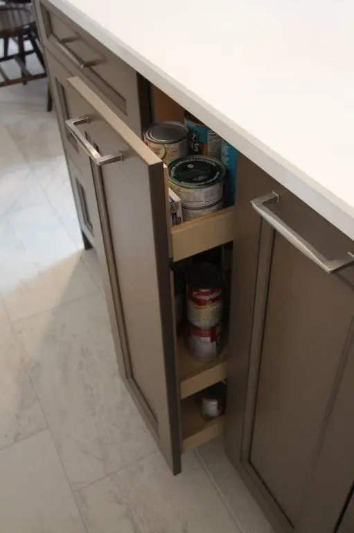 A kitchen pantry cabinet with a pull-out shelf containing canned goods, partially open to show the storage inside.