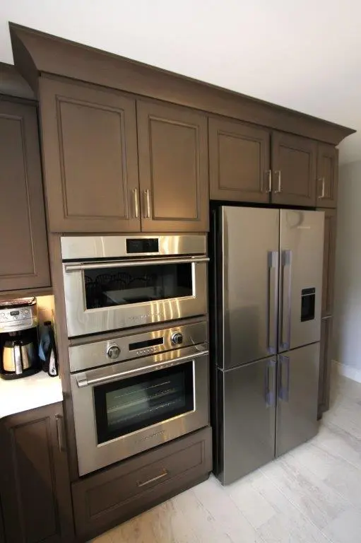 Modern kitchen with stainless steel built-in ovens and a French door refrigerator, surrounded by brown wooden cabinets.