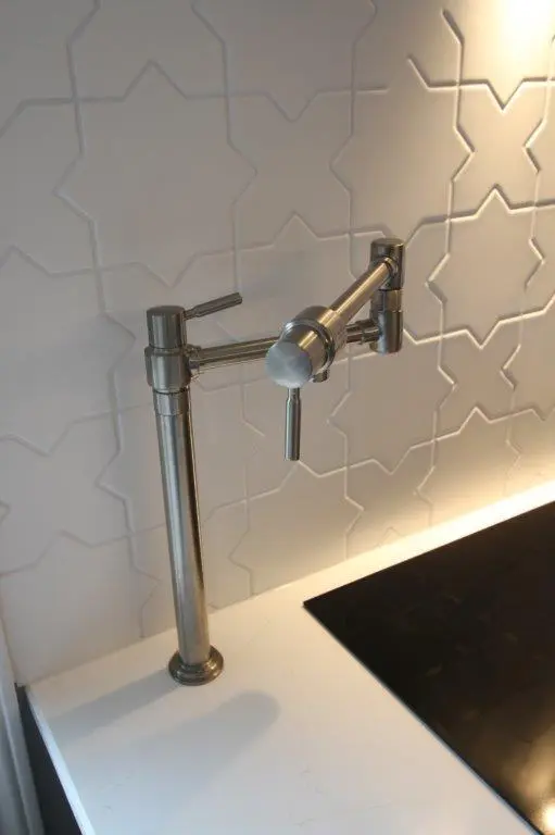 A modern metallic pot filler faucet mounted on a quartz kitchen countertop and tile backsplash with star-shaped tile pattern.
