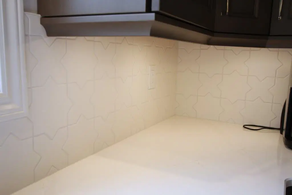 A quartz kitchen countertop with a white star-patterned tile backsplash and dark cabinets above.