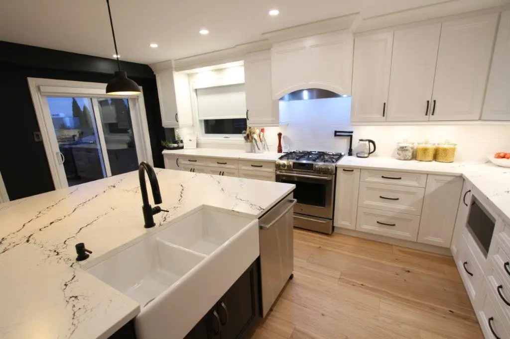 Modern kitchen with white cabinetry, quartz countertops, a central island with a black faucet, stainless steel appliances, and wood flooring.