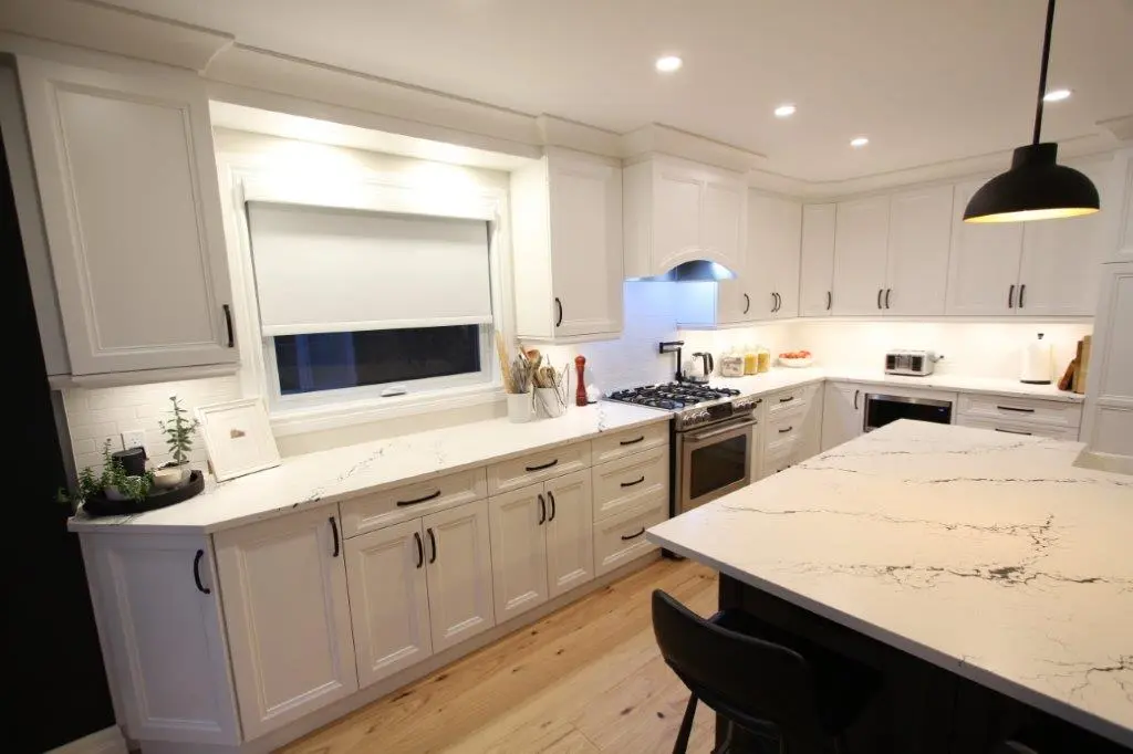 Modern kitchen with white cabinetry, quartz countertops, stainless steel appliances, and a large island with a black pendant light above.
