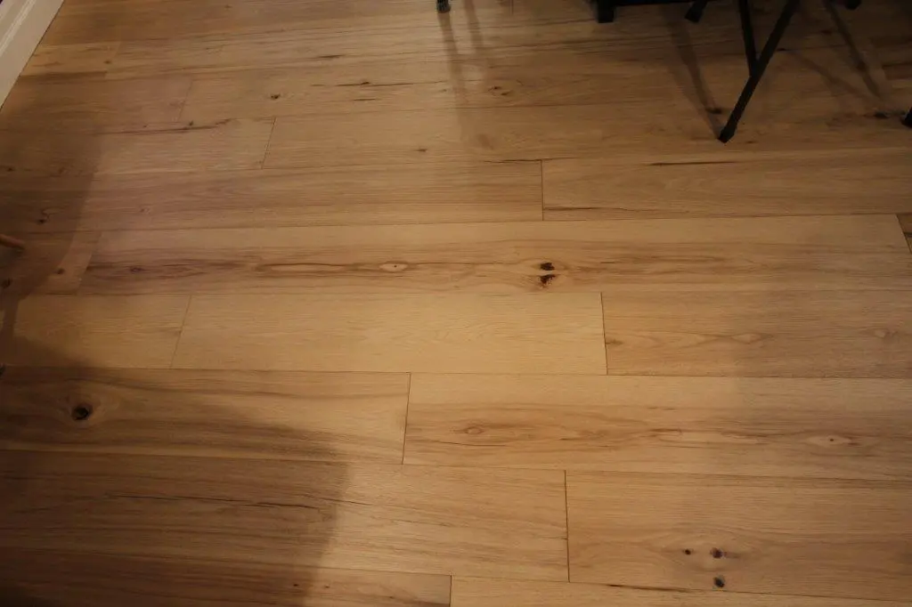 Close-up view of a wooden floor with visible grain patterns and knots, illuminated by warm indoor lighting.