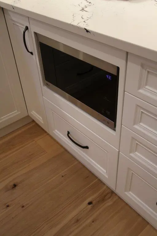 Built-in microwave oven in a white kitchen cabinetry setup with a wooden floor.