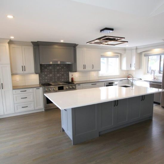 Modern kitchen with white cabinets, a gray island with a quartz countertop, stainless steel appliances, and wooden flooring.