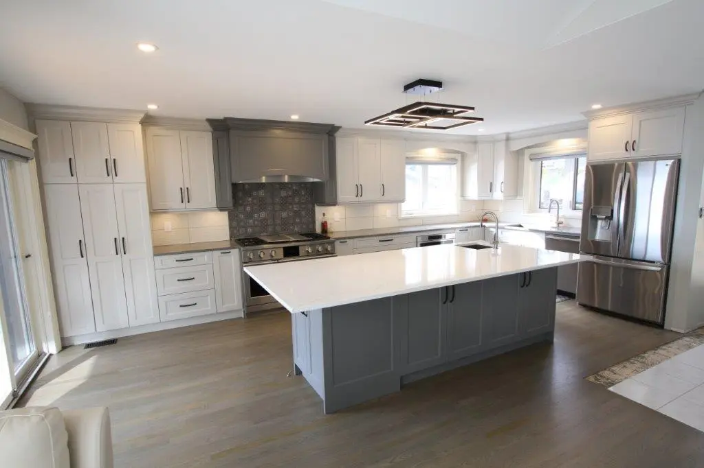 Modern kitchen with white cabinets, a gray island with a quartz countertop, stainless steel appliances, and wooden flooring.