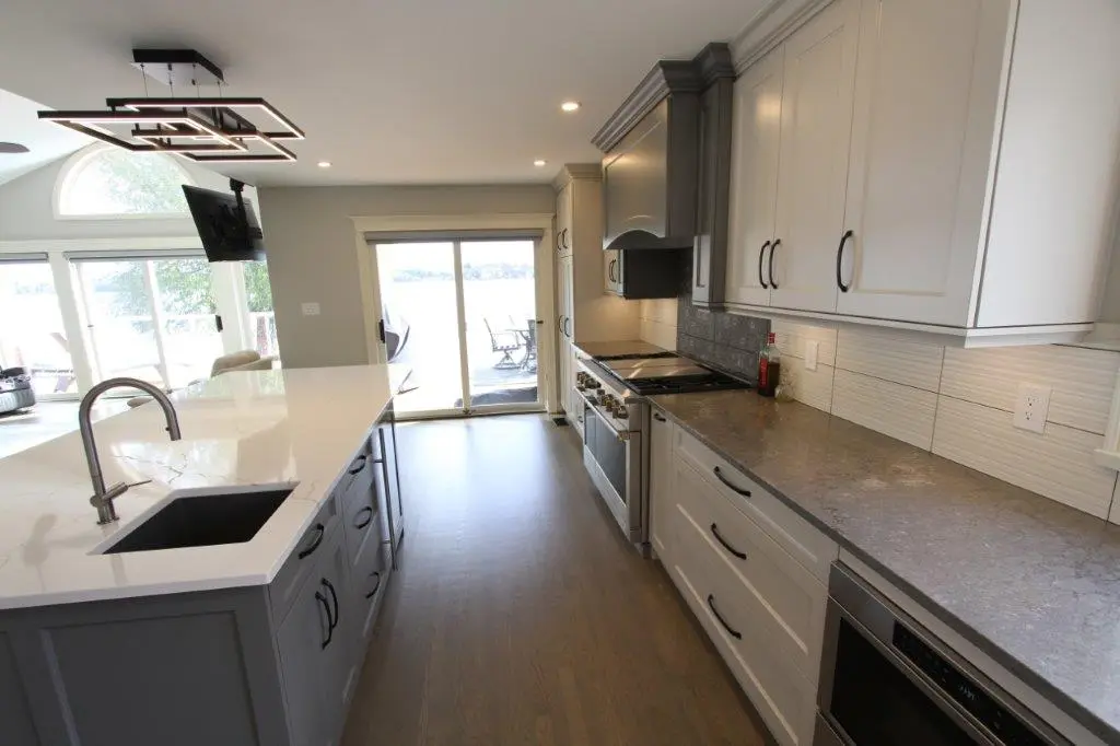 Modern kitchen with gray cabinets, a large white island, stainless steel appliances, and sliding glass doors leading to an outdoor view.