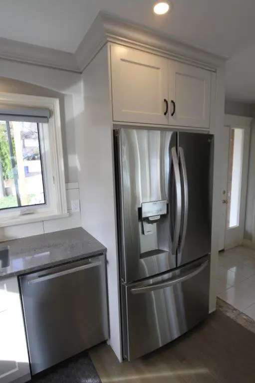 A modern kitchen with a stainless steel French door refrigerator next to grey countertops and white cabinetry.
