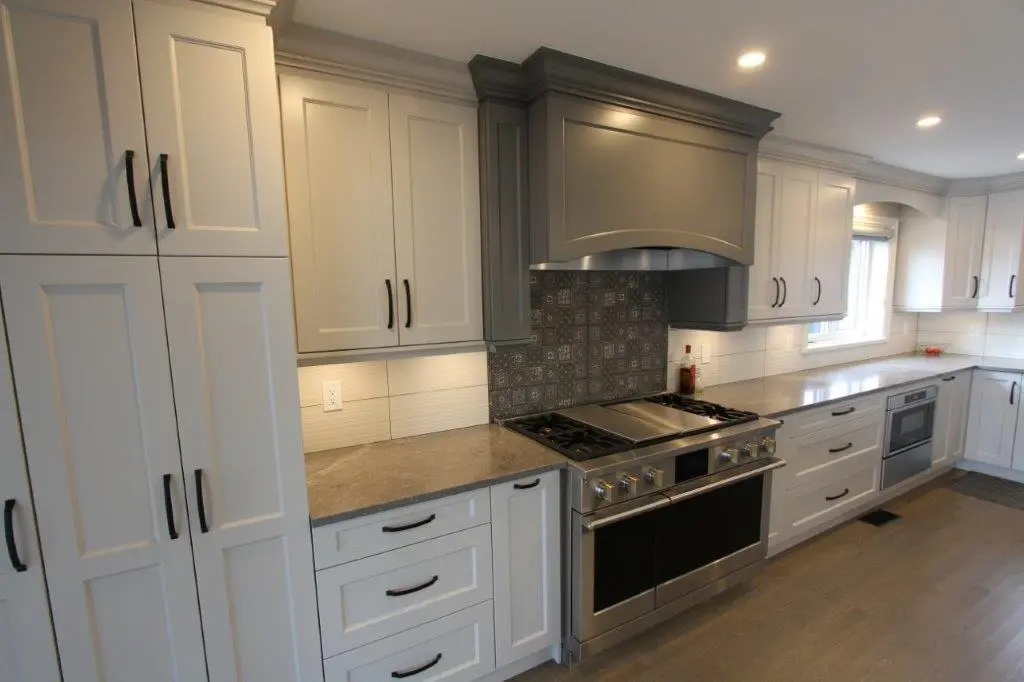 Modern kitchen with light-colored cabinetry, a large stainless steel stove, and a patterned backsplash under a matching hood.