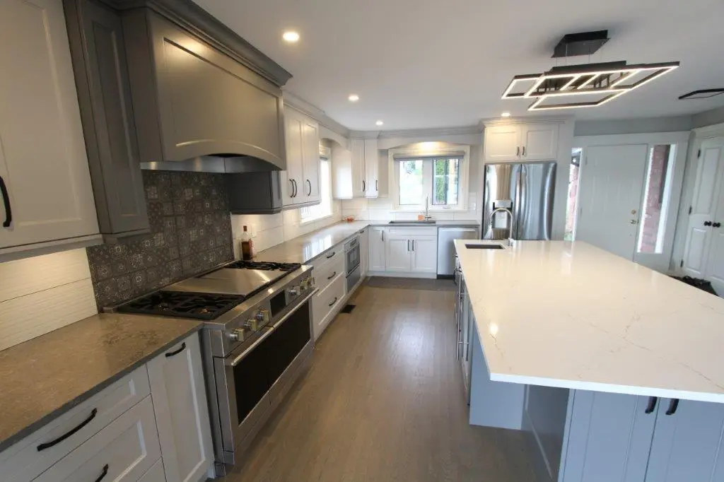 Modern kitchen with gray cabinetry, stainless steel appliances, a large white island countertop, and a patterned tile backsplash.