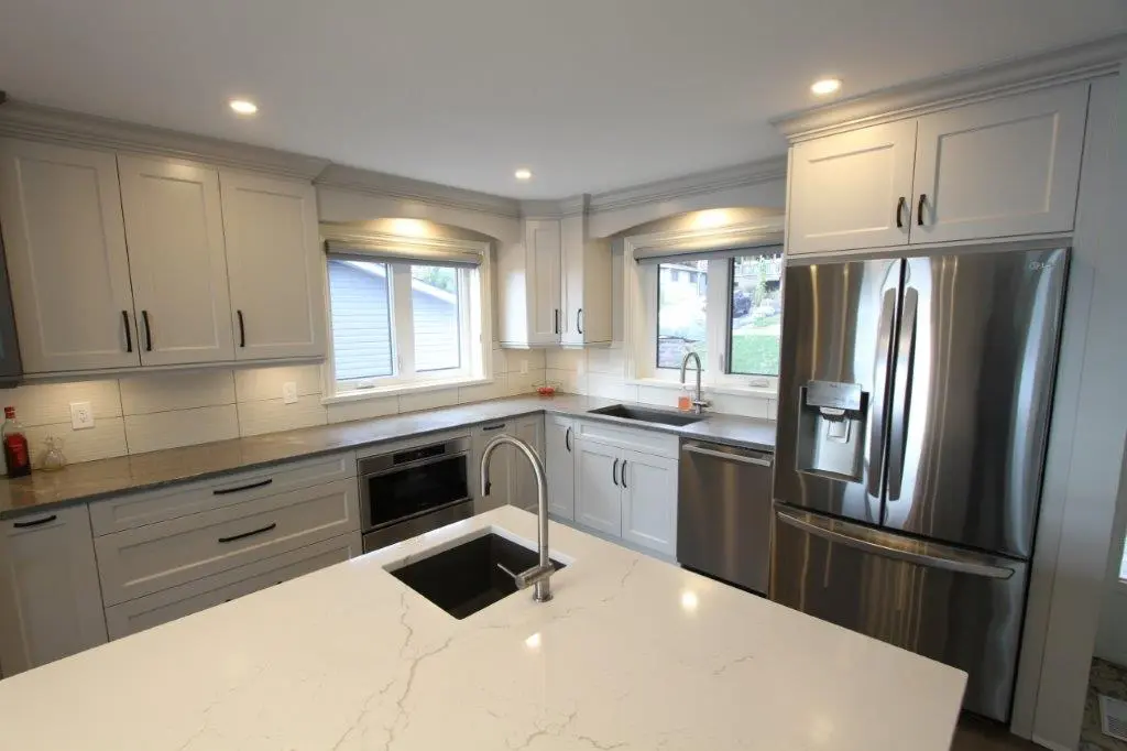 Modern kitchen with white cabinets, stainless steel appliances, and a quartz island countertop with an inset sink.