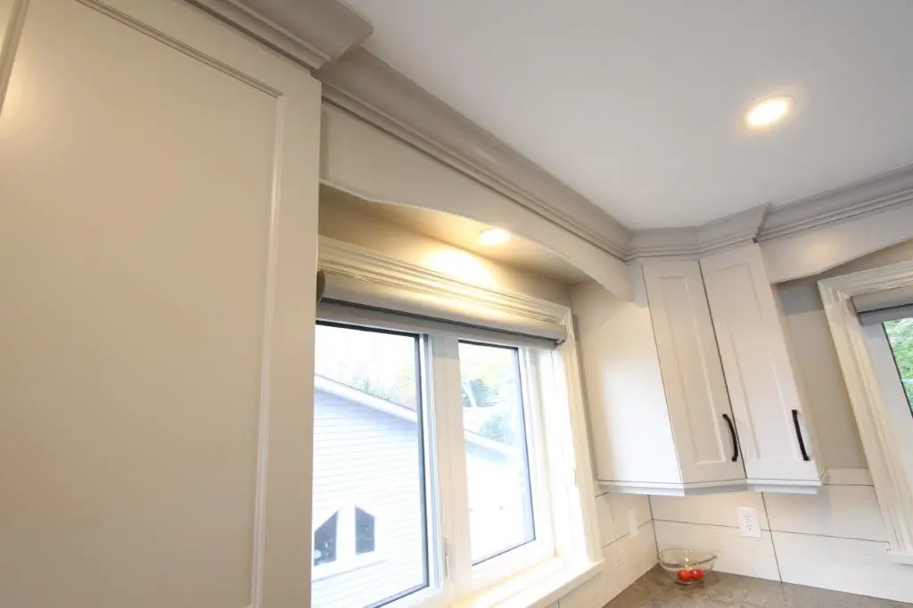 A kitchen corner featuring white cabinets with crown molding, a window with a view of a neighboring house, and recessed lighting.