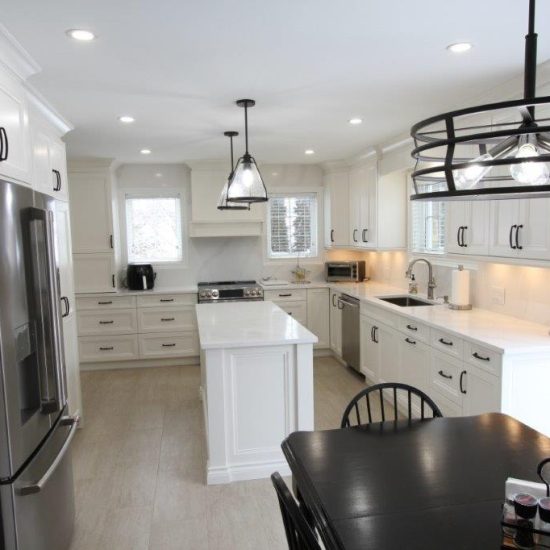 A modern kitchen with white cabinetry, stainless steel appliances, an island with pendant lighting, and a dining table with black chairs.
