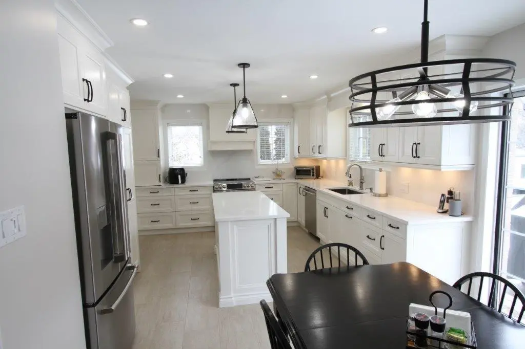 A modern kitchen with white cabinetry, stainless steel appliances, an island with pendant lighting, and a dining table with black chairs.