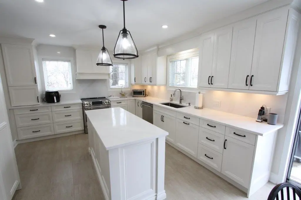 Modern kitchen with white cabinetry, a central island, two pendant lights, and stainless steel appliances.