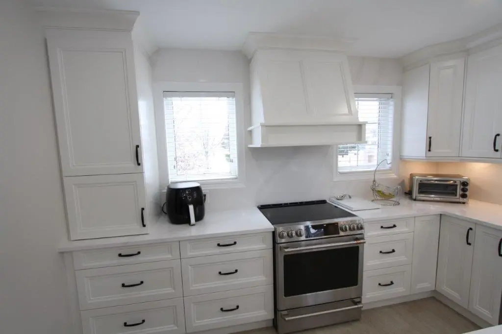 A modern kitchen with white cabinets, a black air fryer, a stainless steel stove, and a toaster oven on the countertop.