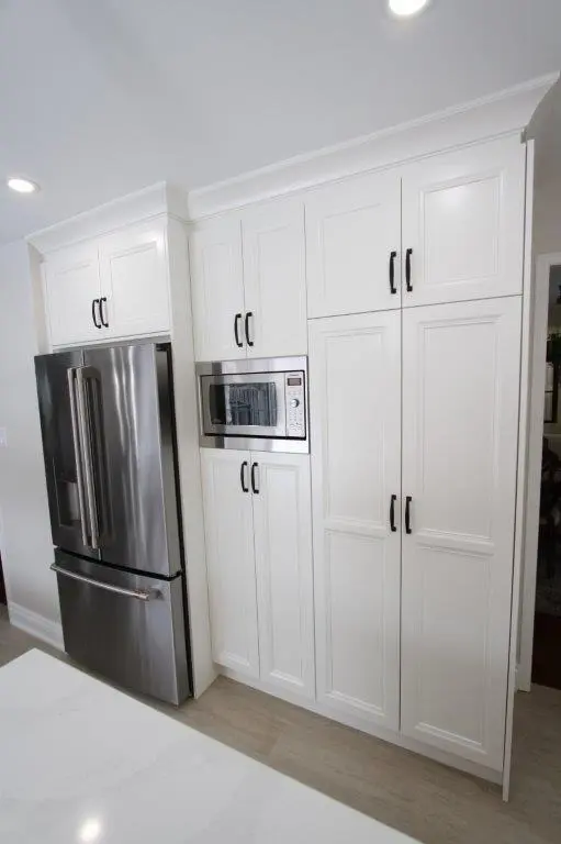 Modern kitchen featuring a stainless steel French door refrigerator and built-in microwave surrounded by white cabinetry with black handles.