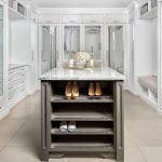 Spacious walk-in closet with white cabinetry, a center island with a marble countertop displaying decorative items, and shelves for shoes.