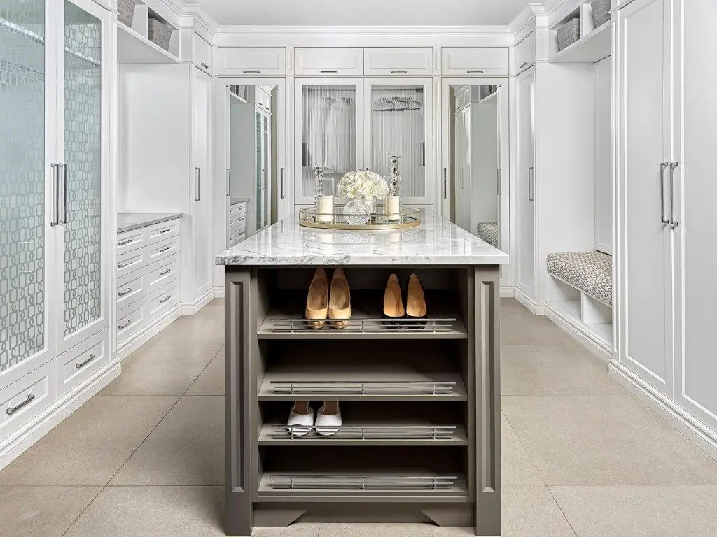Spacious walk-in closet with white cabinetry, a center island with a marble countertop displaying decorative items, and shelves for shoes.