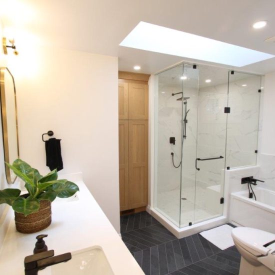 Modern bathroom with a glass-enclosed shower, white porcelain walls, black fixtures, and a white vanity with a plant in a basket.