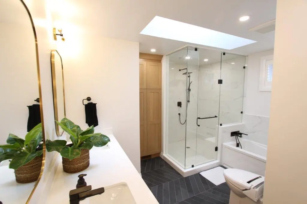 Modern bathroom with a glass-enclosed shower, white porcelain walls, black fixtures, and a white vanity with a plant in a basket.