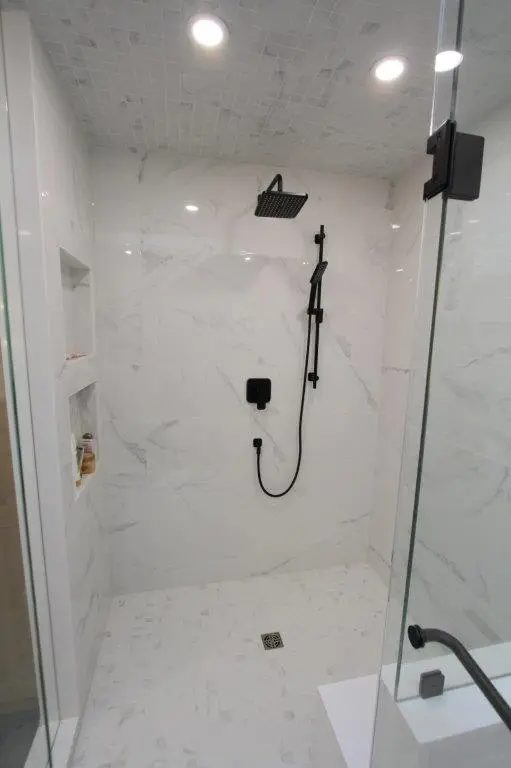 Modern shower with white porcelain tiles, a square black rainfall showerhead, and recessed shelving for toiletries.