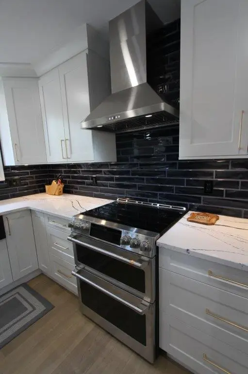 Modern kitchen with white cabinets, a stainless steel range hood, black subway tile backsplash, and a stainless steel oven with a glass cooktop.