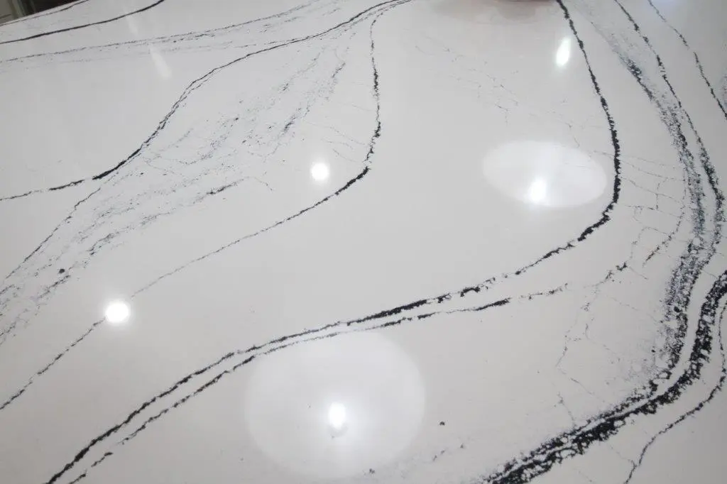 Close-up view of a white quartz surface with dark, curving veins and reflections of ceiling lights.