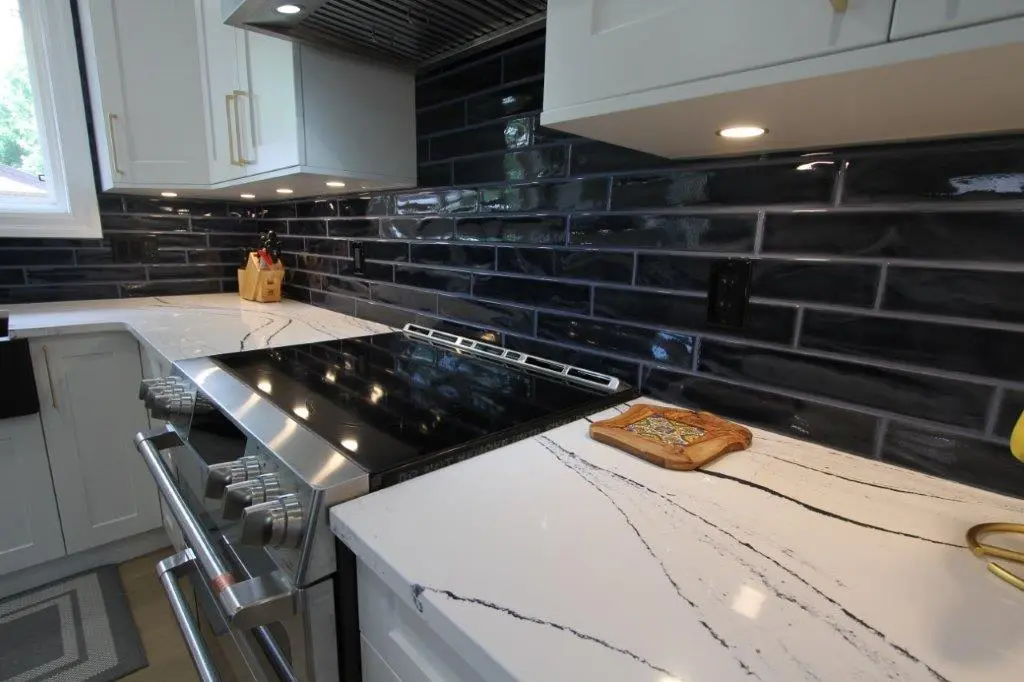 Modern kitchen with white quartz countertops, a stainless steel stove, and dark subway tile backsplash.