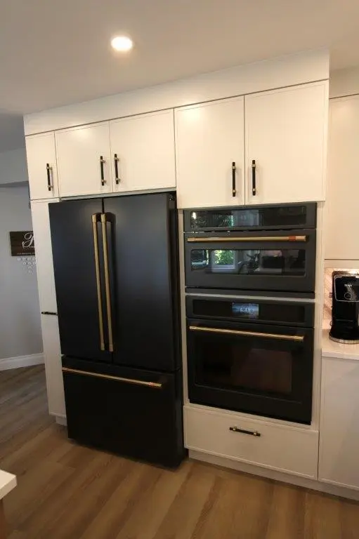 A modern kitchen featuring a black French door refrigerator and double wall oven integrated into white cabinetry with black handles.