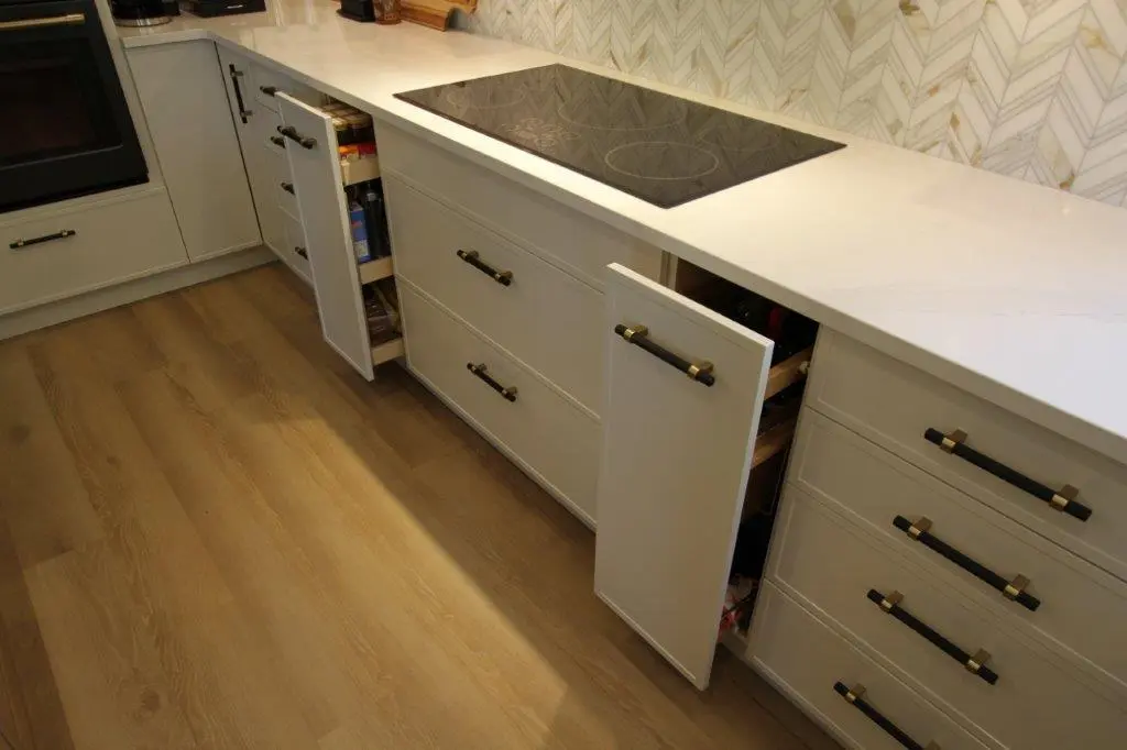 Modern kitchen with white cabinets, black handles, an electric stovetop, and open drawers and cabinets revealing storage space.
