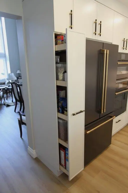 A kitchen with a pull-out pantry next to a refrigerator, containing various food items on shelves.