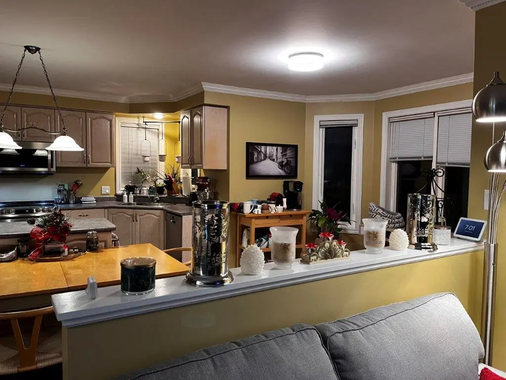 A before renovation kitchen and dining area with a warm color scheme, featuring wooden cabinets, a dining table with chairs, and decorative candles and ornaments on a dividing countertop.