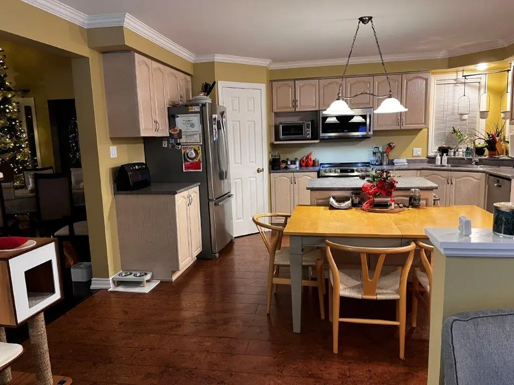 A before renovation kitchen with wooden cabinets, a stainless steel fridge, a dining table with chairs, and pendant lights overhead.