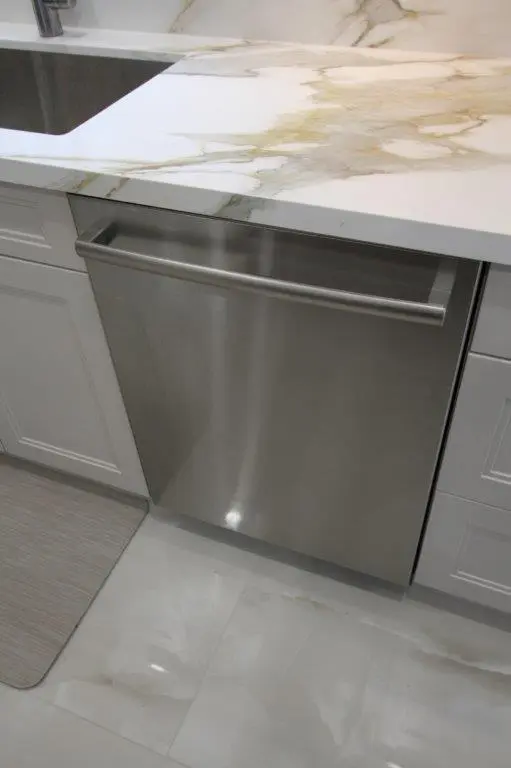 Stainless steel dishwasher integrated into a modern kitchen with porcelain countertop and white cabinetry.