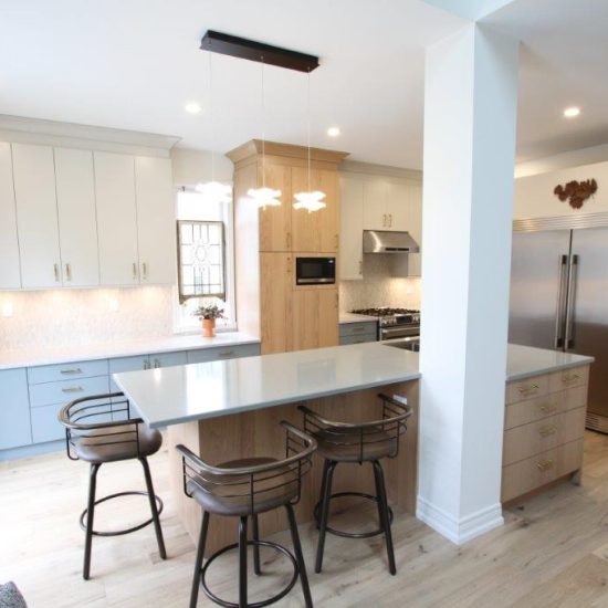 Modern kitchen with light wood flooring, a large island with bar stools, white and blue cabinets, and stainless steel appliances.